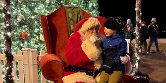 Santa with child in chair by lit Christmas tree