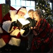 Santa opening lit book in front of kid and mother